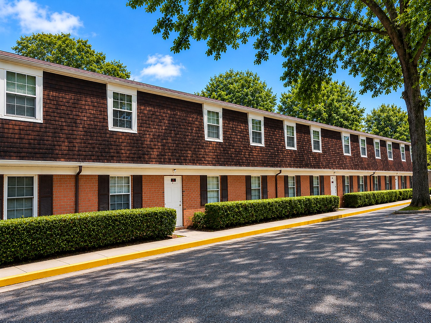 Red Oak Apartments row of brick homes with trees, hedges, and blue sky
